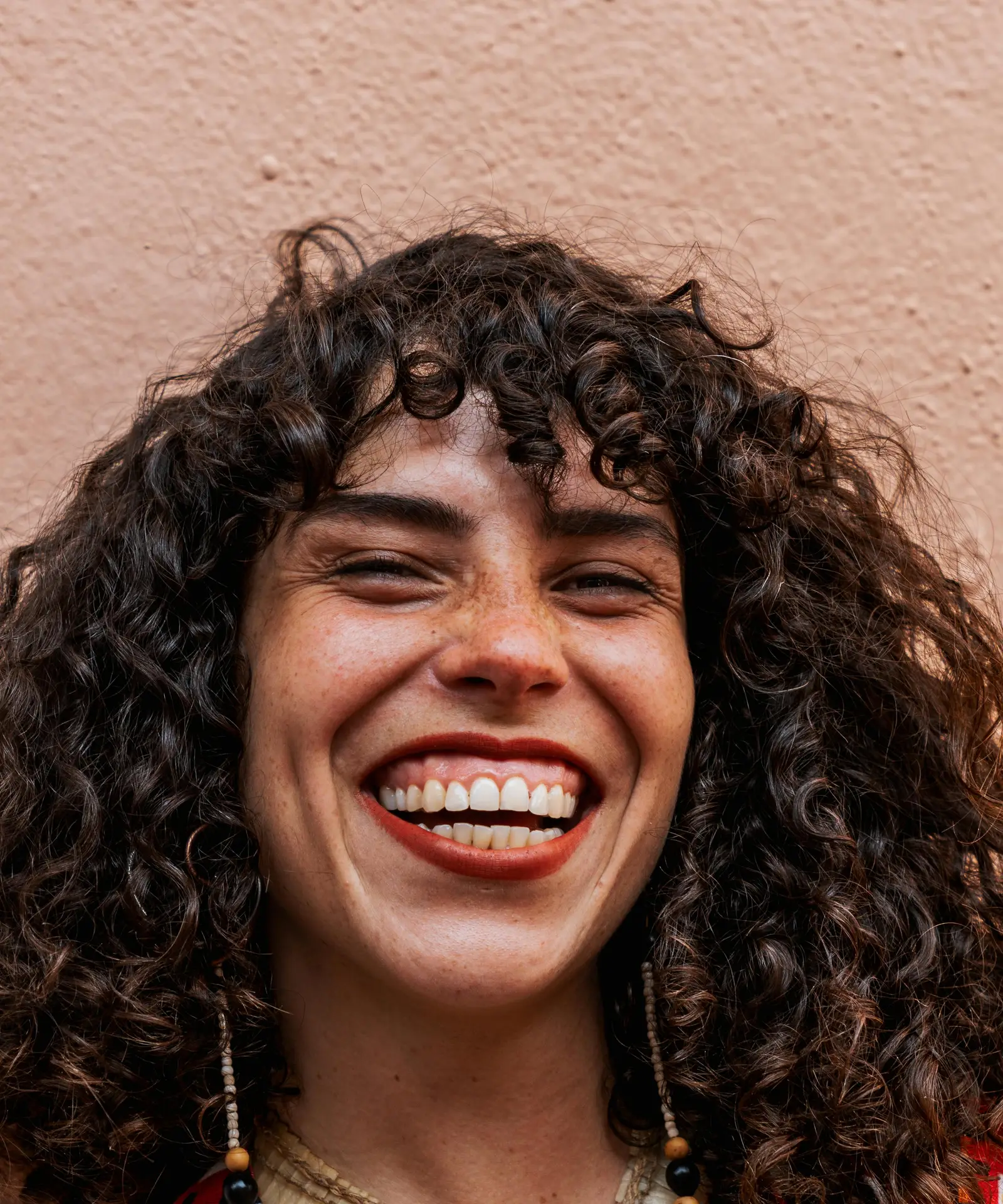 Happy woman with curly hair, bold necklace, and colorful outfit smiling outdoors.